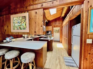A wooden cabin interior with a kitchen area, bar stools, and a refrigerator.