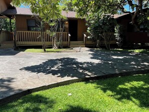 A wooden house with a porch, surrounded by lush greenery and a concrete pathway. - Hale Kahakai ~ 2 BR ~ Ocean Front - Puako (Waimea)
