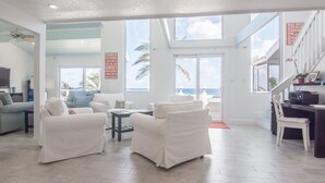 Amplia sala de estar con muebles blancos, un televisor y vista al océano.