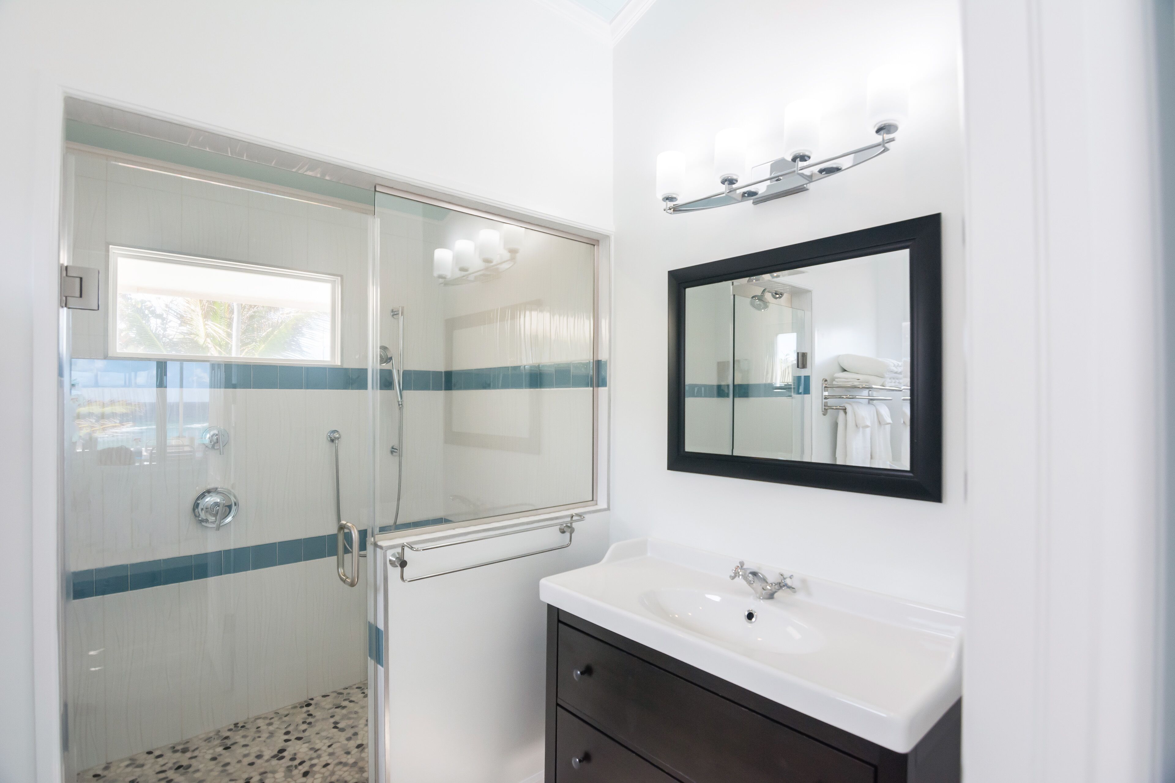 A bathroom with a glass-enclosed shower, a white sink with a dark cabinet, and a mirror with lights above it.