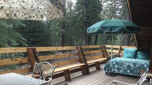 Eine Holzterrasse mit Tisch, Stühlen und einer Bank, sowie ein Bett mit einem grünen Baldachin.