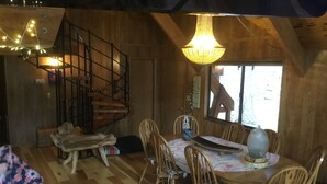 Ein gemütliches Holzinterieur mit Esstisch, Stühlen, einer Treppe und einem Kronleuchter.