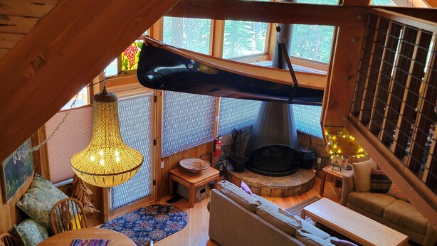 Ein gemütliches Blockhaus-Interieur mit einer Holztreppe, einem Kamin, einem Essbereich und einer Sitzecke mit Kissen.