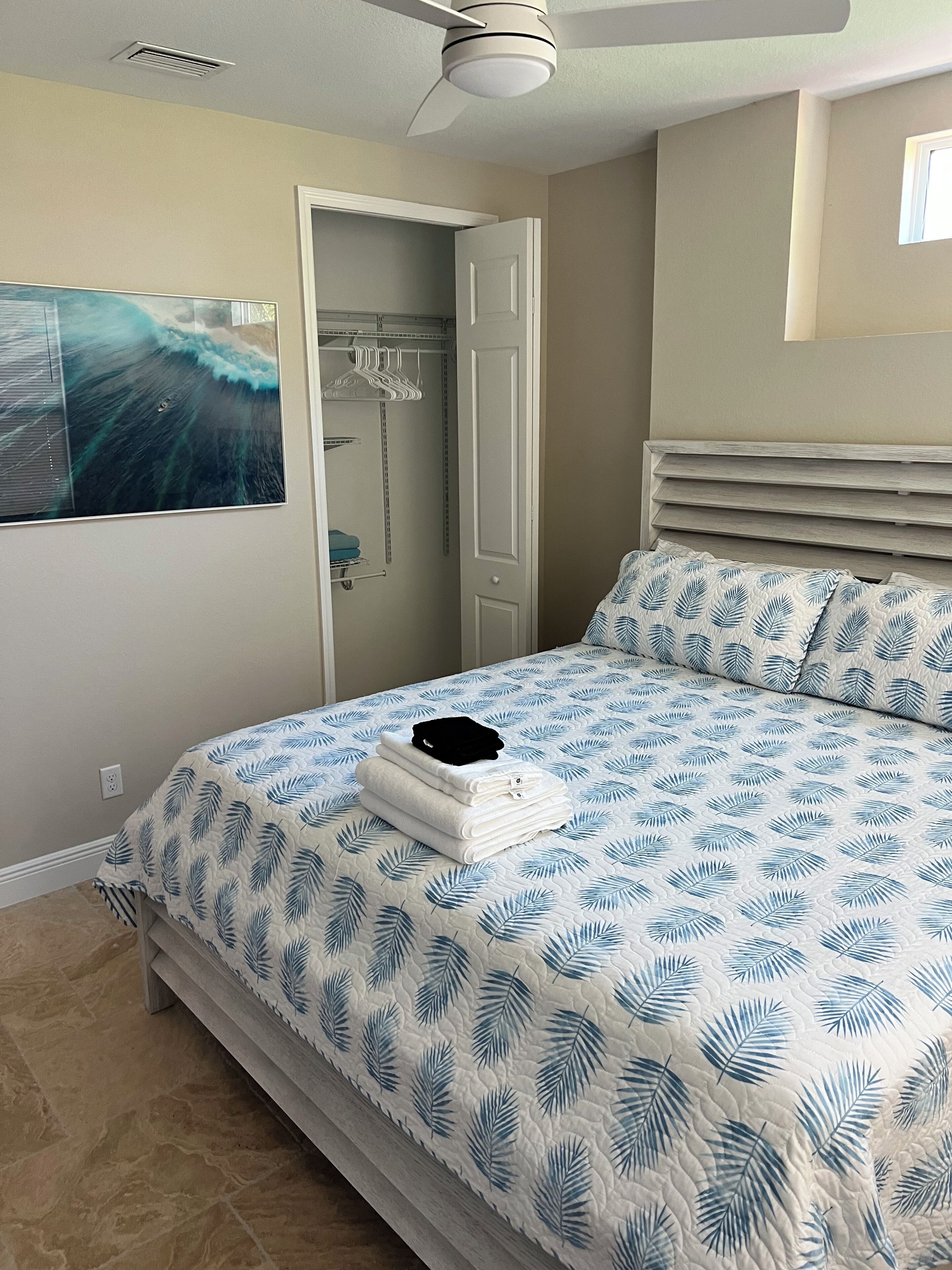 Un dormitorio con una cama, ventilador de techo, una puerta y un cuadro en la pared.