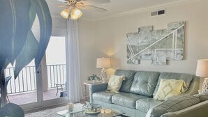 Ein Wohnzimmer mit grauem Sofa, einem Couchtisch, einem Deckenventilator und einer großen Pflanze.