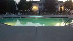 Una piscina con un jacuzzi, rodeada de sillas de descanso y un edificio al fondo.