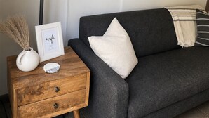 Ein modernes Wohnzimmer mit einem dunkelgrauen Sofa, einem hölzernen Nachttisch mit Lampe, einem gerahmten Bild und einer Wanddekoration.