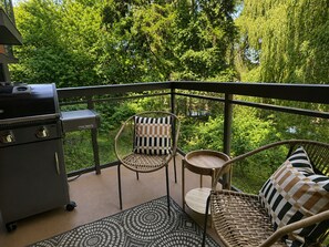 Un balcón con una parrilla, sillas de mimbre y vistas a vegetación exuberante.