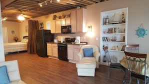 Een knus woongedeelte met een kitchenette, een eethoek met een stoel en tafel, een bank en een bed.