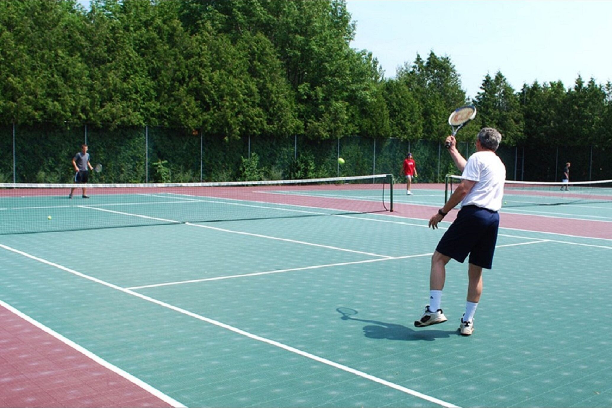 An outdoor tennis court with a net, surrounded by trees.
