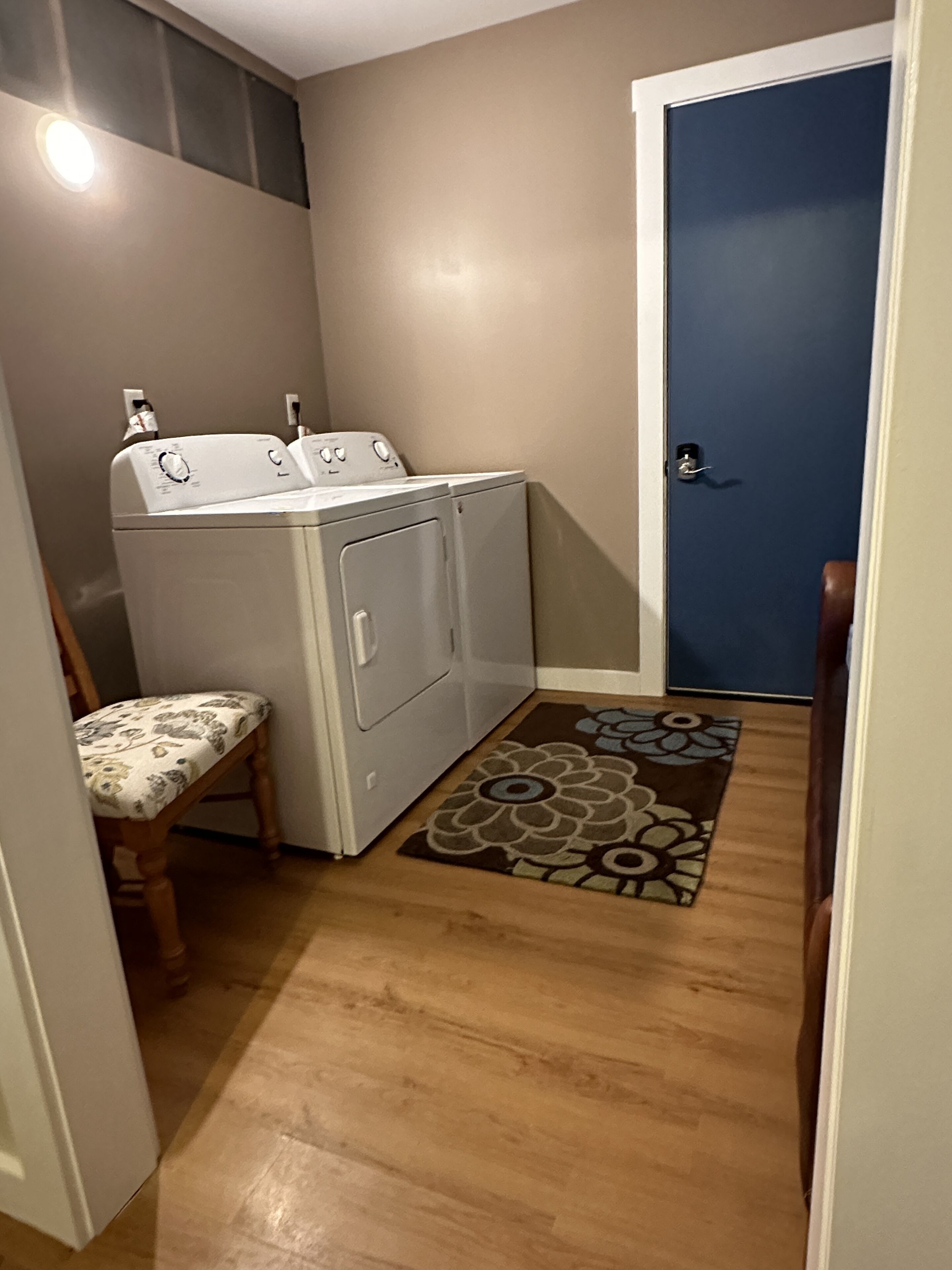 A laundry room with a washing machine, a chair, and a patterned rug.