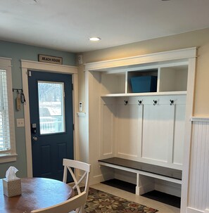 A room with a blue door, a bench, and a white wall-mounted shelf with hooks.