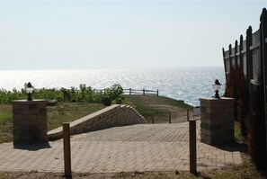 A paved pathway leading to a coastal area with a fence and lamp posts.