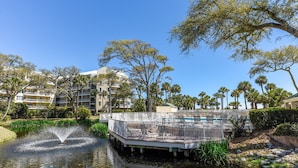 A waterfront view with a pool, palm trees, and a building with balconies. - Modern 5th Floor Villa w/ Panoramic Views (Hilton Head Island)