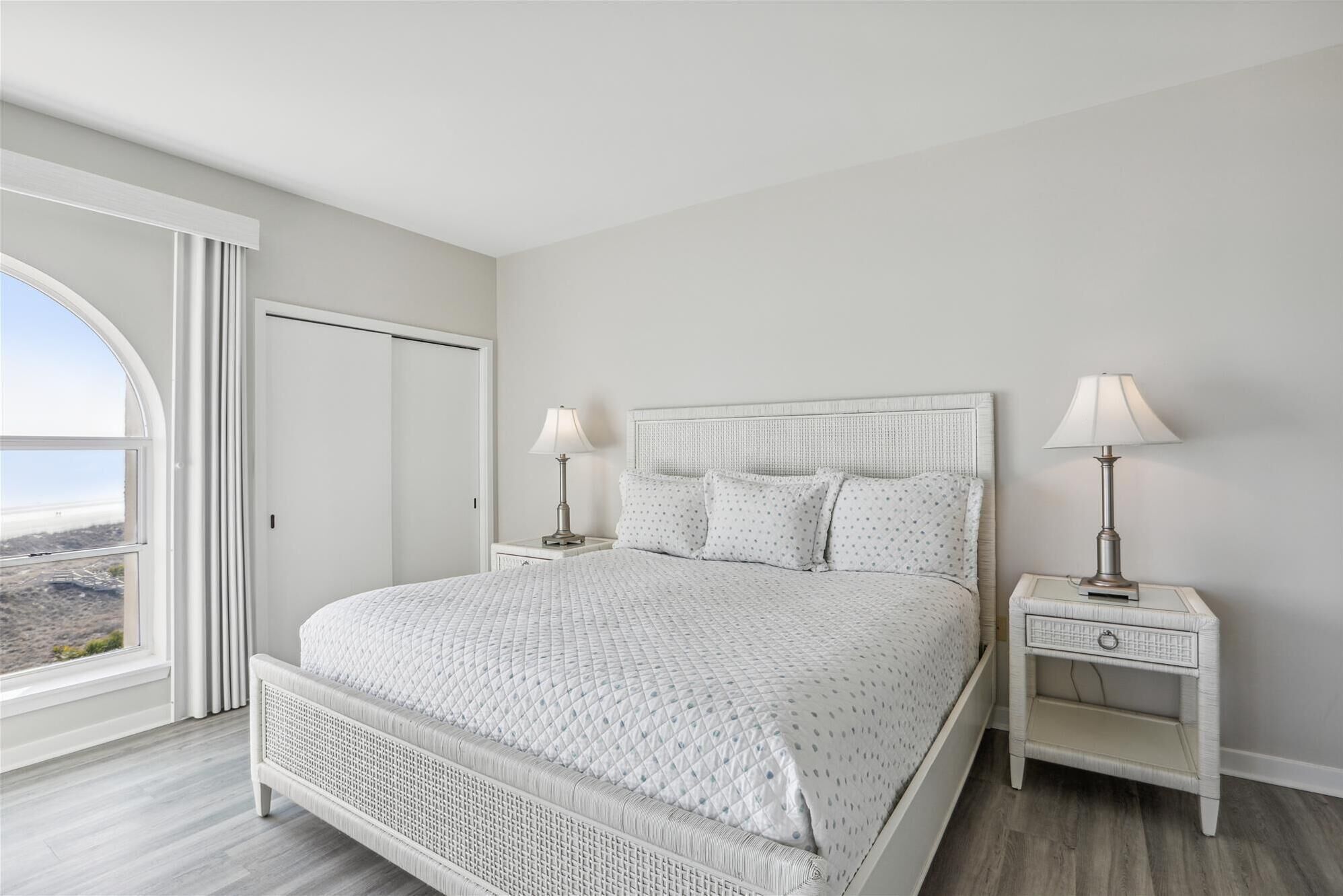 Una camera da letto con un letto grande, due comodini con lampade, un armadio e vista sull'esterno attraverso una grande finestra.