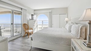 A bedroom with a large bed, a chair, a TV, and a balcony with a view. - Modern 5th Floor Villa w/ Panoramic Views (Hilton Head Island)