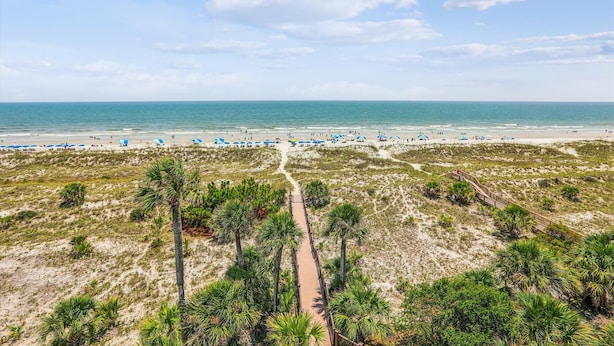 A beach with a wooden boardwalk, beach umbrellas, and sparse vegetation. - Modern 5th Floor Villa w/ Panoramic Views (Hilton Head Island)