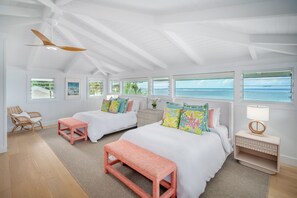Ein Schlafzimmer mit zwei Betten, einem Deckenventilator und großen Fenstern mit Blick aufs Meer.