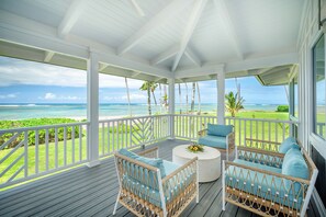 Ein überdachter Außenbereich mit Korbmöbeln, einem runden Tisch und Blick auf das Meer und den Strand.