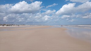Una playa amplia de arena con olas suaves, cielo despejado y algunas nubes dispersas.