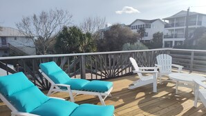 Una terraza de madera con sillas reclinables blancas y una mesa, rodeada por una barandilla de madera.