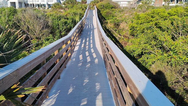 Un paseo marítimo de madera que conduce a propiedades frente a la playa, con vistas al océano.