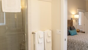 A bathroom with a glass shower enclosure, a white towel hanging on the wall, and a wooden floor. - Two Master-King Suites+! (Sonoma)