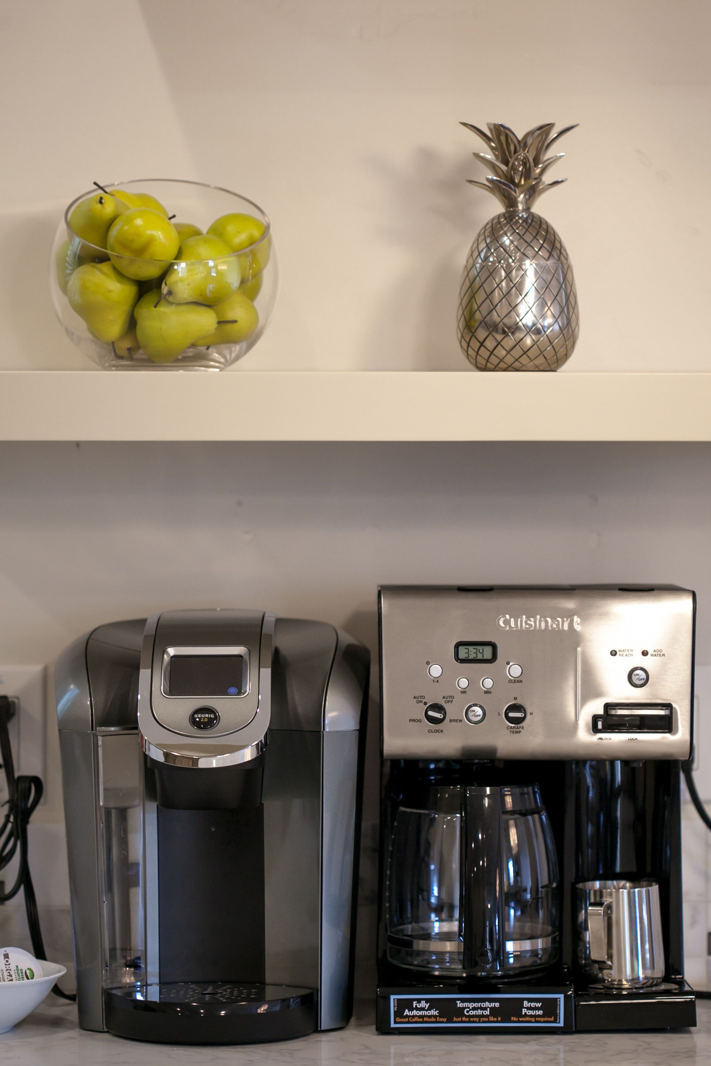 Una cocina con una cafetera y un bol de manzanas verdes sobre la encimera.