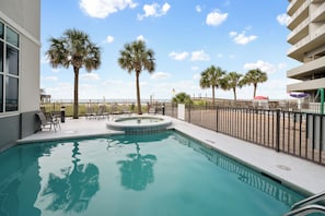 Piscina con jacuzzi, rodeada de palmeras y vista a la playa.