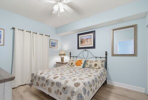 Un dormitorio con cama, mesita de noche, lámpara y ventilador de techo.
