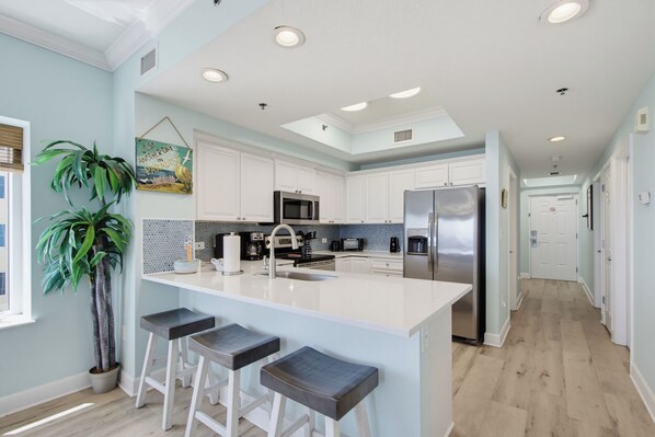 A modern kitchen with white cabinetry, a central island with bar stools, a stainless steel refrigerator, and a microwave.