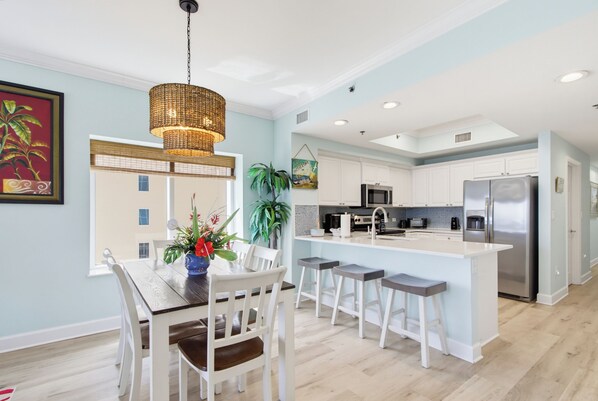 Una cocina moderna con armarios blancos, una isla central con taburetes de bar, una lámpara colgante y un comedor con mesa y sillas.
