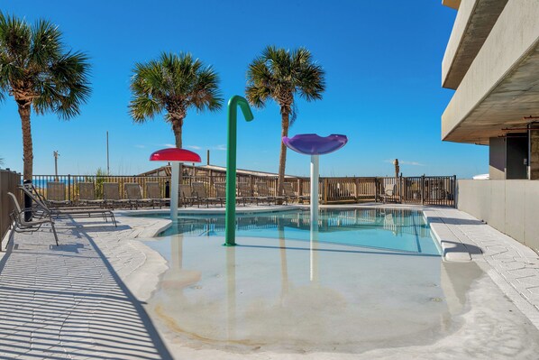 A swimming pool with a clear blue water surface, surrounded by lounge chairs and palm trees.