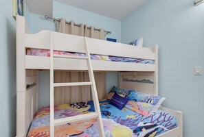 Una cama litera con escalera, una cama inferior con una colcha colorida y una cama superior con cortina.