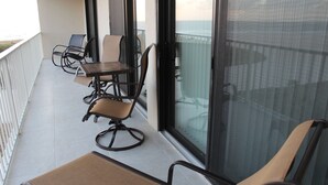 A balcony with a table and chairs, large windows, and a view of the sea.