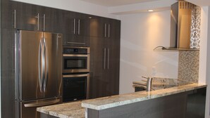 A modern kitchen with a stainless steel refrigerator, double ovens, and a granite countertop.