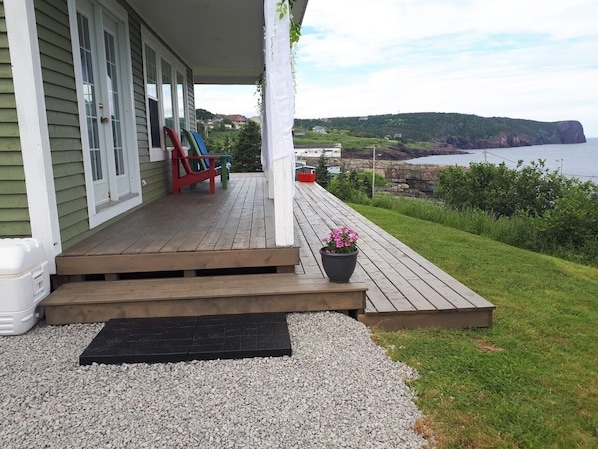 A wooden deck with steps leading to a house with green siding and white trim. A red chair and a potted plant are on the deck.