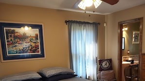 A bedroom with a bed, a ceiling fan, a painting, a window with curtains, and a wooden floor. - Beautiful Lakefront Getaway (Cedar Bluff)