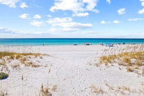 Een strand met wit zand, weinig gras en een helderblauwe lucht.