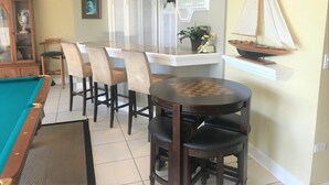 A pool table, bar stools, a dining table, and a sailboat model in a room with a tiled floor and a window with shutters. - Bay Front - 'Villa La - Vue', Incredible Bay & Golf Course Views!  Sleeps 15. (Miami Beach)