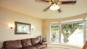 A room with a brown leather sofa, a wooden coffee table, a ceiling fan, and a large window with a view of trees. - Bay Front - 'Villa La - Vue', Incredible Bay & Golf Course Views!  Sleeps 15. (Miami Beach)