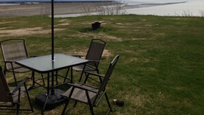 An outdoor seating area with a table and chairs under a large umbrella, overlooking a body of water.
