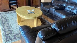 A living room with a leather sofa, a wooden coffee table, a TV, a cabinet, and a patterned rug.