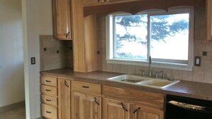 A kitchen with wooden cabinets, a double sink, and a window with a view of trees.