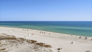 Una amplia playa de arena con cielo azul despejado y mar tranquilo.