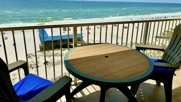 Una terraza con una mesa redonda y dos sillas, con vista a una playa y una vista despejada del océano.