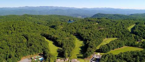 An aerial view of a forested area with a golf course, a lake, and distant mountains.