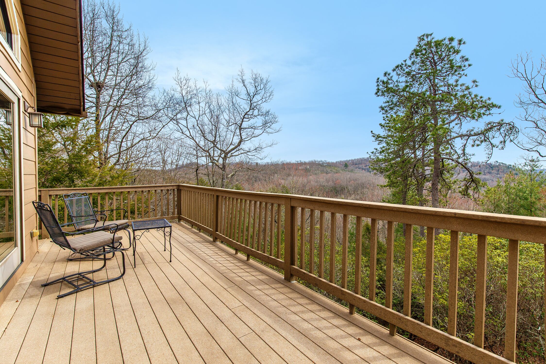 A wooden deck with two chairs and a table, overlooking a forested landscape.