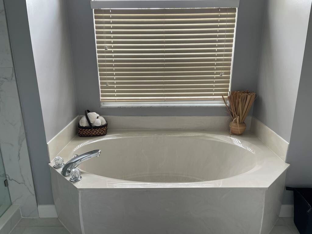 Un baño moderno con una bañera independiente, un ventanal con persianas y una pequeña cesta de artículos de aseo.
