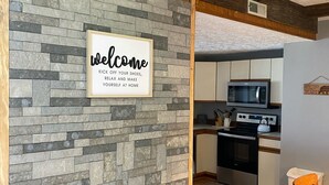 Una cocina moderna con un muro de acento de piedra, un cartel de bienvenida y un techo de madera.